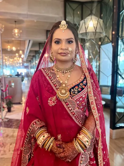 A full-length portrait of the bride. The rich red of her outfit is paired with a golden-toned makeup look that exudes royalty and grace.
