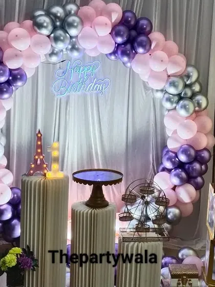 A simple ring decoration with purple, pink, and silver balloons against a white curtain.