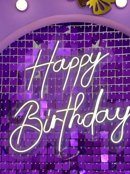 A close-up of a "Happy Birthday" neon sign mounted on a vibrant purple sequin wall. This shows how I can customize the color of the shimmer wall to match any party theme.