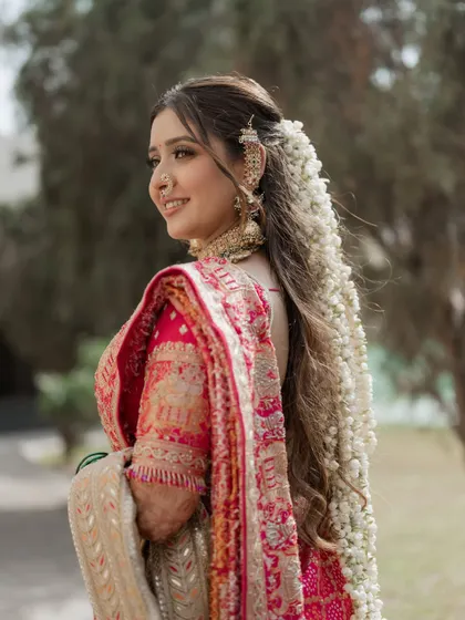 This look is a symphony of love and tradition. The bride is wearing a stunning pink bandhani saree, and I’ve complemented it with soft, glowing makeup and an elaborate hairstyle featuring a cascade of fresh flowers.