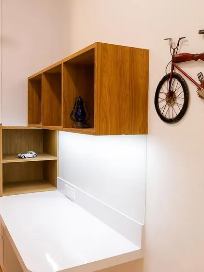 A minimalist study corner in Richa and Abhay's home, featuring a clean white desk, wooden shelving, and a fun bicycle wall art piece.