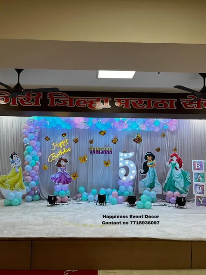 An L-shaped balloon arch with a princess theme for a 5th birthday. The stage is decorated with cutouts of various princesses and a large light-up number '5'.