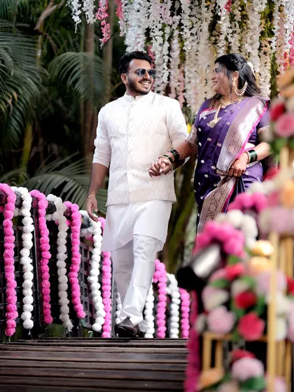 The couple walks hand-in-hand across a beautifully decorated bridge. This shot captures the movement and grandeur of the wedding procession, framed by floral arrangements.