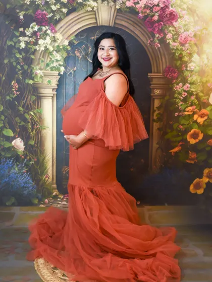 A smiling portrait of a mom-to-be in a rust-colored gown against our floral arch backdrop.