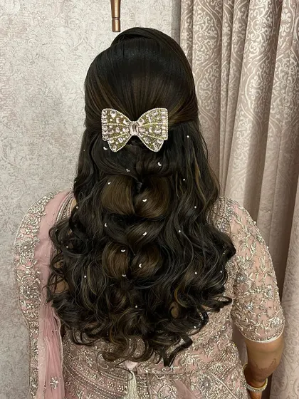 A fun and glamorous half-up style with bouncy curls. The look is completed with a large, sparkling bow accessory and scattered pearls.
