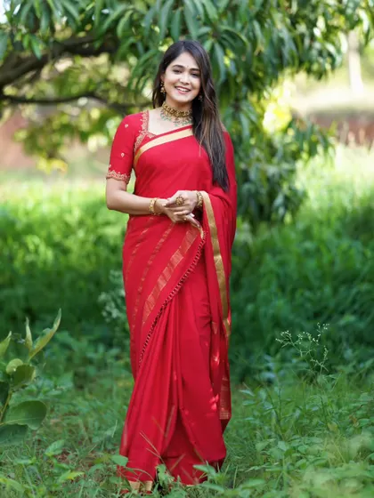 The vibrant red saree stands out beautifully in this natural, outdoor setting.
