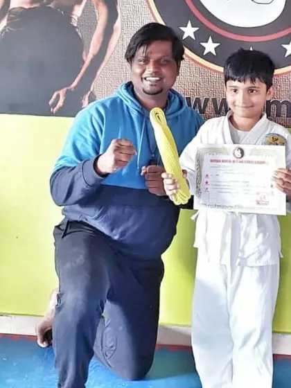 A young boy is all smiles as he receives his yellow belt and certificate, marking a successful belt test.
