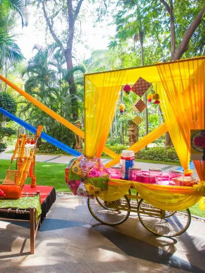 A beautifully decorated food cart at an outdoor event, draped in colorful yellow and blue fabrics. This can be used to serve anything from welcome drinks to desserts.