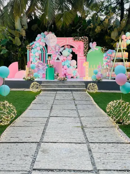 A grand outdoor setup for a first birthday, with a stone pathway leading to a beautiful stage in pastel pinks and blues.