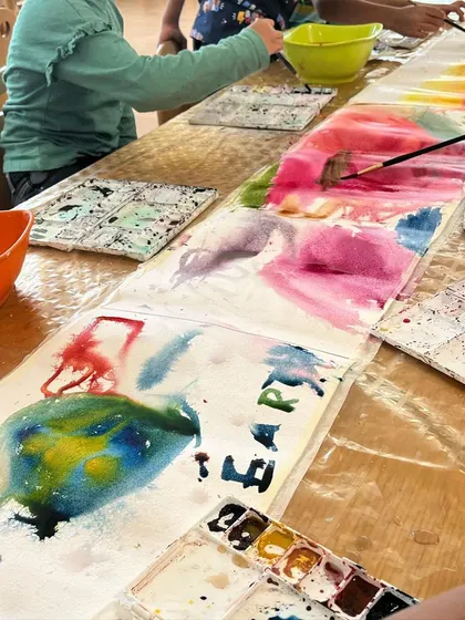 A long table of young artists, each absorbed in their own watercolor creation. We provide a shared space for individual exploration.