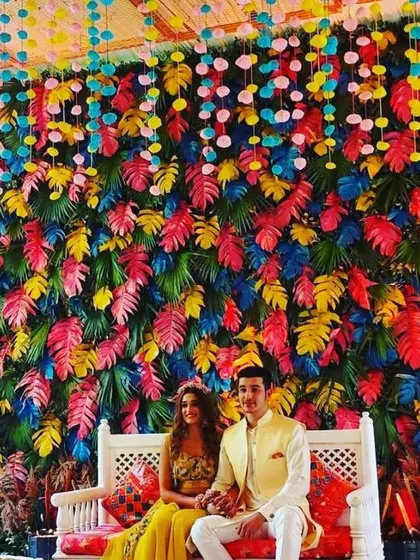 A unique and modern photo backdrop featuring a wall of multi-colored tropical leaves. This creative and colorful setup provides a stunning background for couple portraits and guest photos, adding a contemporary touch to any wedding event.
