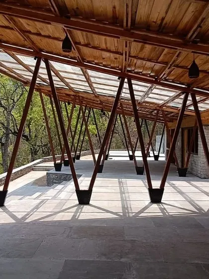 **Angling Centre, Pancheshwar:** The V-shaped wooden columns create a rhythmic, forest-like colonnade. This structural system is both functional and expressive, echoing the surrounding trees and creating a dynamic play of shadows on the stone floor.