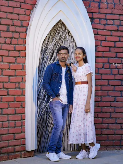 A stylish couple's portrait against a red brick wall with a unique arched doorway.