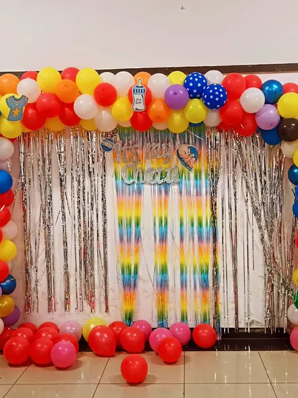 A vibrant and colorful setup for a "Chatti" ceremony, a traditional event celebrating a newborn. The rainbow balloon arch and shimmer curtain create a joyful and festive atmosphere for this important family ritual.
