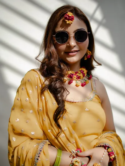 The perfect mix of tradition and modern style. Bride Nidhi looks radiant in her sunglasses and floral jewelry for her Haldi ceremony.
