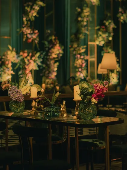 A high-top table at the emerald Sangeet, surrounded by lush, moody florals and soft candlelight, perfect for evening conversations.