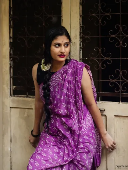 A classic pose against an old-world door with intricate grilles. The model's expression is poised and direct, and the setting adds a vintage charm to this ethnic portrait in a purple saree.