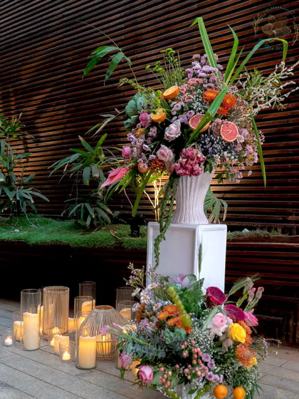A large, dramatic floral installation for an outdoor event. The mix of tropical flowers and citrus fruits creates a vibrant and abundant look, perfect for a celebration.