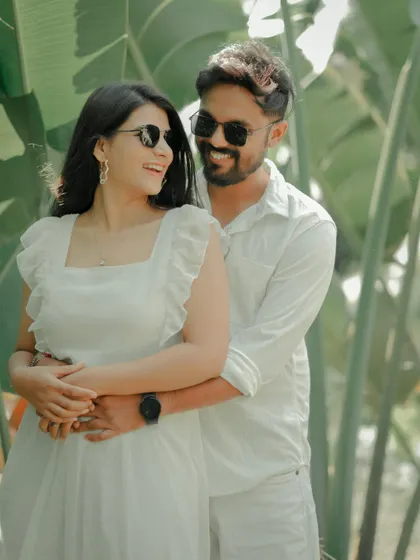 A fun and carefree moment captured against a backdrop of lush tropical leaves. The couple, dressed in matching white, shares a laugh, showcasing the relaxed and joyful side of their relationship.