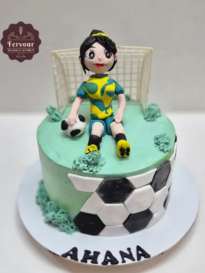 A football cake for a female player, featuring a hand-molded fondant figure sitting on the field. The sides of the cake are decorated with a soccer ball pattern.