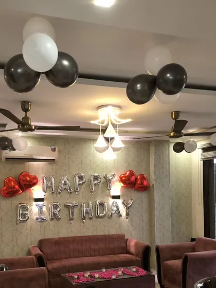 A clear shot of the living room setup with silver "Happy Birthday" foil letters and black and white balloon clusters.