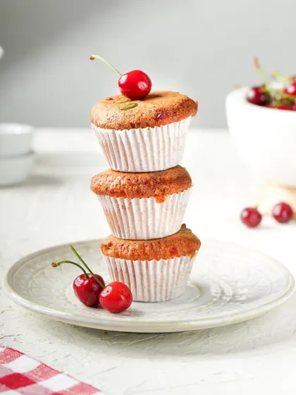 A playful stack of three cherry-topped muffins. The bright, clean background and simple styling make this a classic and appealing shot for any bakery.