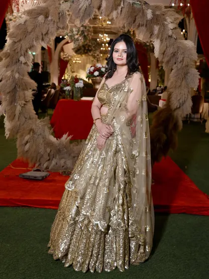 A full-length shot of the guest in her golden lehenga, posing against a beautiful wedding decor backdrop.