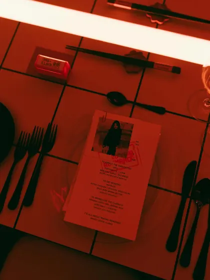 The table setting for Rohan's 30th, featuring a personalized menu with his photo, set against a modern, tiled tabletop under red neon light. The vibe was cool, personal, and a little bit extra.