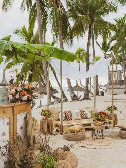 A lounge area on the beach in Mauritius, featuring rustic wooden pallet sofas and tropical print cushions.