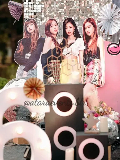 A decor detail from a K-Pop party, featuring a cutout of the girl group Blackpink. The setup includes '6' marquee lights and speaker props, perfect for a fan's birthday.