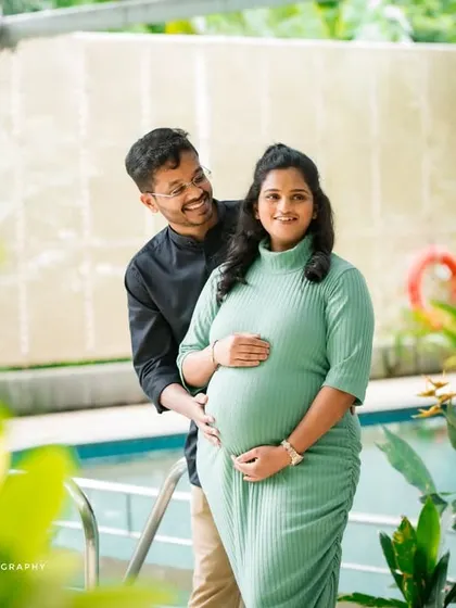 A joyful portrait of an expecting couple by a pool. The mother-to-be is wearing a lovely light green dress, and the focus is on their happy connection.