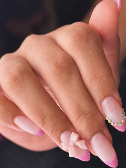A sweet and elegant design combining a pink French manicure with a sculpted 3D bow and a delicate line of crystals. It’s a perfect example of a feminine and detailed nail enhancement.