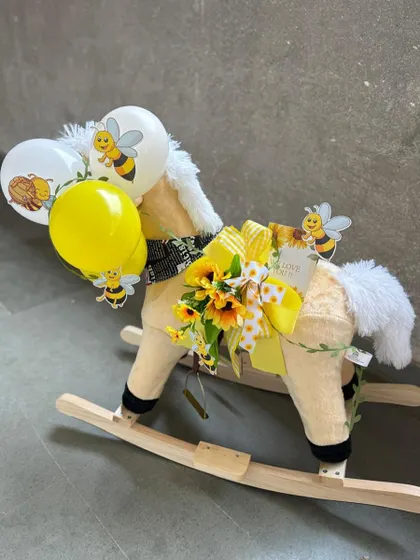 A whimsical and grand gesture for a baby announcement. We've transformed a classic rocking horse into a stunning gift platform, adorned with a bee-themed balloon bouquet and other sweet surprises.