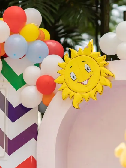 A smiling sun peeking over a colorful balloon arch at our Cocomelon party. It's these small, cheerful details that come together to create a happy and immersive environment for a child's special day.