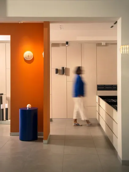 The layout is designed for easy navigation, with clear sightlines through different zones. This view captures the interplay of color, from the orange wall to the blue pedestal, against a clean, white canvas.