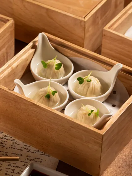 A clean, minimalist shot of soup dumplings in a wooden box. The simple composition draws all attention to the food itself.