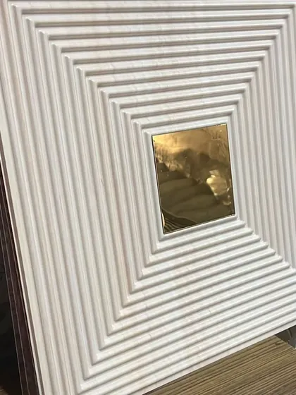 A white PVC panel with a grooved texture and a gold mirror center, seen from an angle to show its 3D quality.