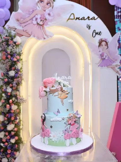 The cake display for 'Anara's Onderland' birthday. The two-tiered cake is perfectly framed by lighted arches and floating fairy cutouts.