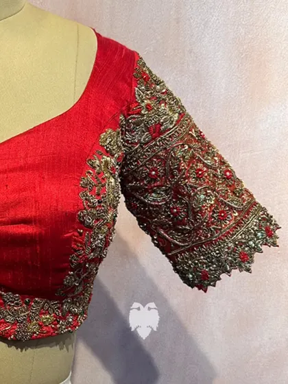 A close-up of the sleeve of Madhavi's deep maroon raw silk blouse, adorned with arched motifs of peacocks and florals.
