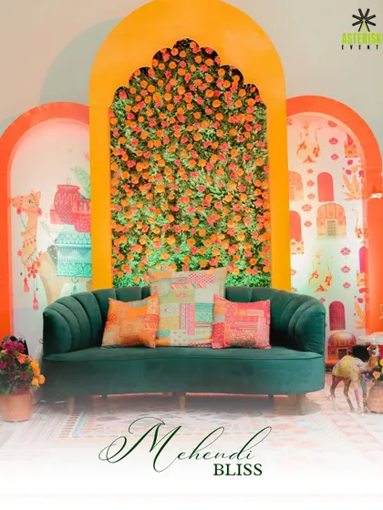 A beautiful Mehendi seating area with a backdrop of marigold flowers. The plush green sofa provides a stunning contrast to the warm orange tones, creating a rich and inviting look.