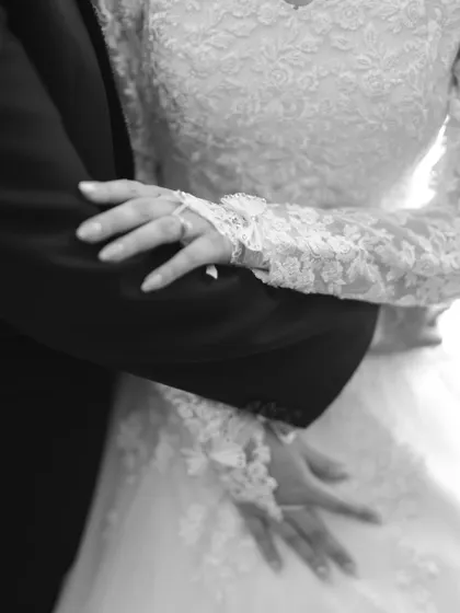 A black and white detail shot of the couple's hands and the bride's lace sleeve.