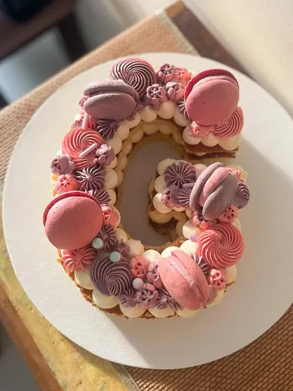 Letter cakes are a fun and personal way to celebrate. This 'G' monogram cake is decorated with beautiful monochrome buttercream swirls in shades of pink and purple, topped with matching macarons.