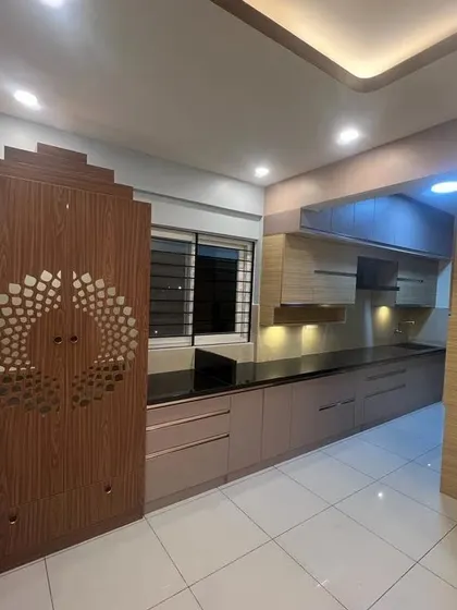 A kitchen and pooja unit combination in a newly completed apartment. The kitchen features a long counter with modern cabinets, seamlessly flowing from the living area.