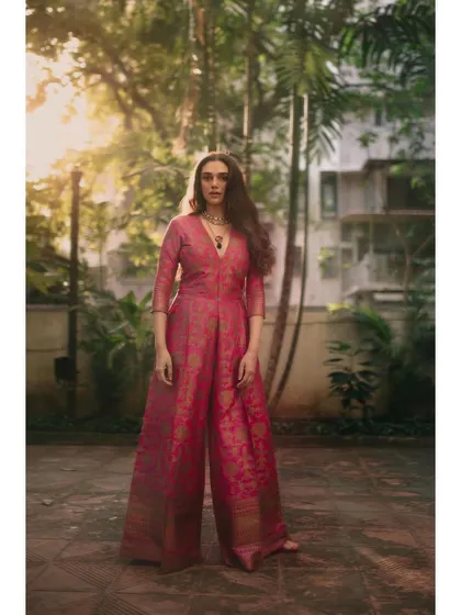 The full-length view of the pink brocade jumpsuit. The wide-leg pants and V-neck create a flattering and comfortable fit.