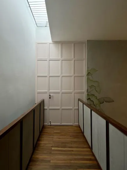 The skylit bridge connecting the two wings of the upper floor. The wooden flooring and simple railings are illuminated from above, creating a bright and uplifting passageway.