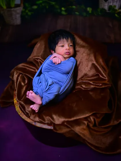 A simple and sweet newborn photo. The baby is wrapped snugly in a blue swaddle, resting on a soft brown blanket.