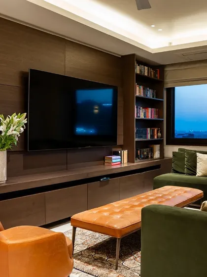 A TV lounge area designed for comfort and style. The deep green sofa is paired with a vibrant orange armchair and a leather ottoman, showcasing our ability to use color and texture to define a space.