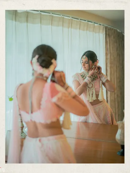 The bride getting ready, adjusting her earrings in the reflection of a mirror.