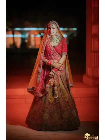 A full-length portrait of the bride in her red and gold lehenga, looking radiant.