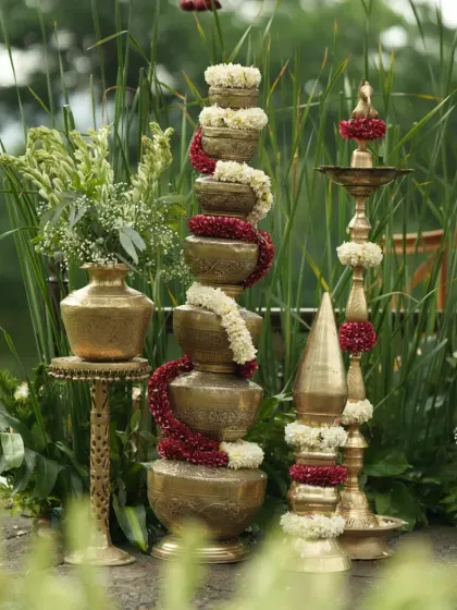 A wider view of the traditional brass decor, including the stacked pots and various diyas, arranged artfully against a natural green backdrop.
